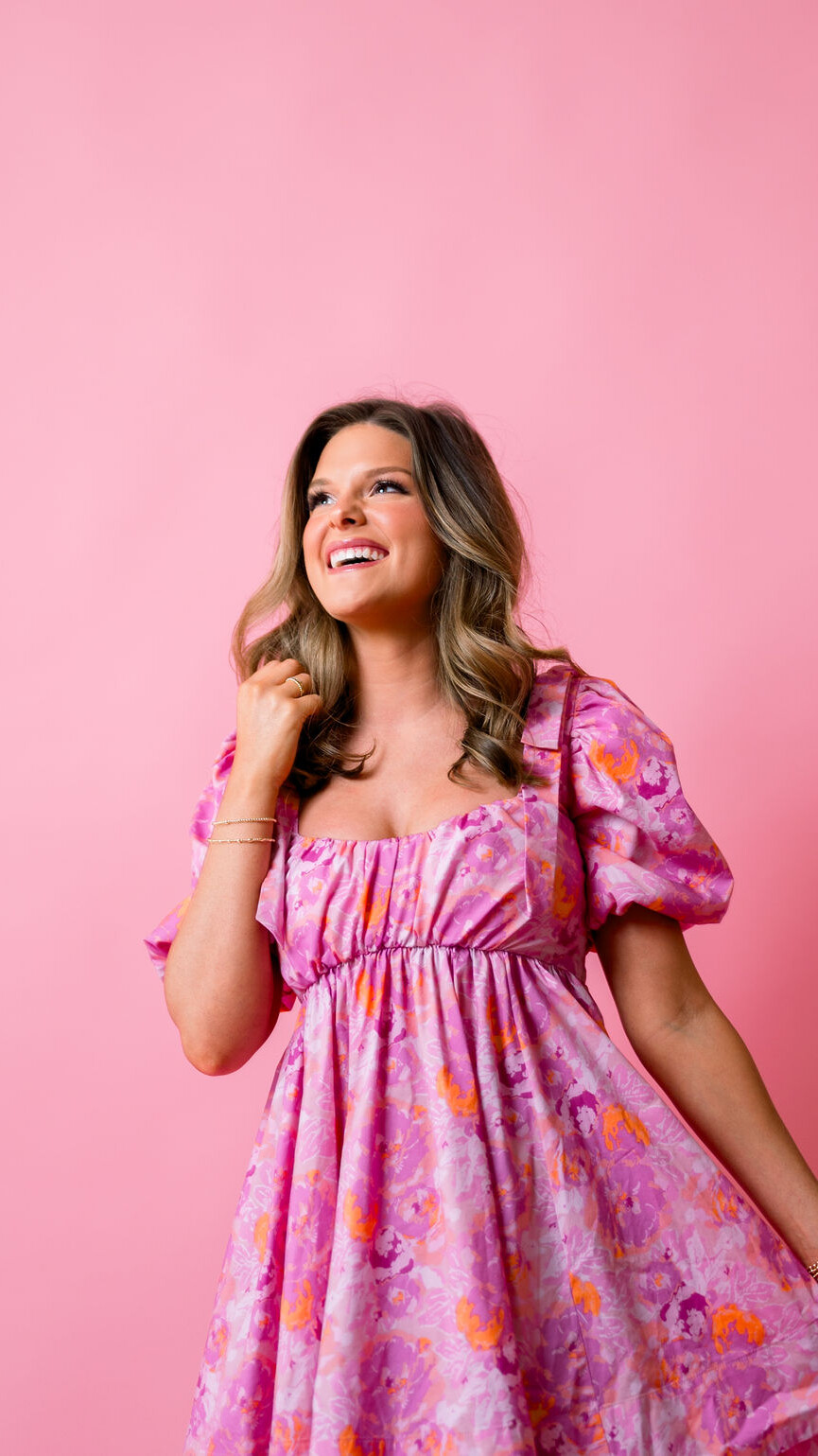 Girl with a happy aspirational look in pink dress in front of a pick backdrop